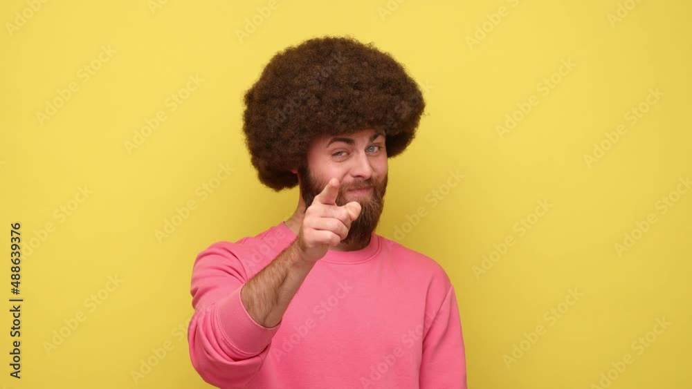 Bearded man looking with incredulous suspicious gaze and touching nose, gesturing you are liar, suspecting falsehood, wearing pink sweatshirt. Indoor studio shot isolated on yellow background. Bearded man looking with incredulous suspicious gaze and touching nose, gesturing you are liar, suspecting falsehood, wearing pink sweatshirt. Indoor studio shot isolated on yellow background.