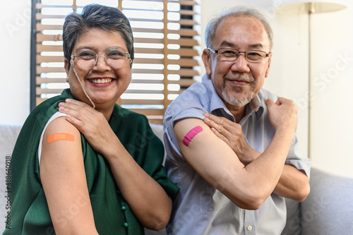 Healthy Asian senior couple showing bandage plaster on arm after received covid vaccination for prevent covid-19 infection. Coronavirus pandemic protection health care senior lifestyle concept.