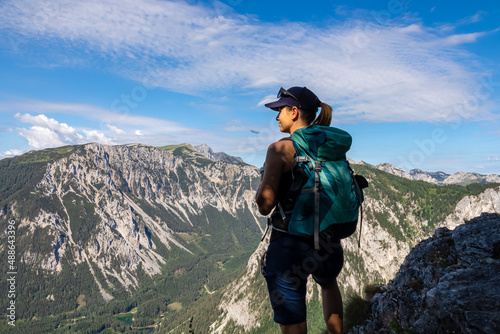 Woman with a hiking backpack standing on the rock with a panoramic view on the alpine mountain chains in Austria, Hochschwab region in Styria. Freedom and adventure vibes. Oberort, Tragoess. Summer