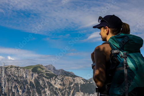 Woman with a hiking backpack standing on the rock with a panoramic view on the alpine mountain chains in Austria, Hochschwab region in Styria. Freedom and adventure vibes. Oberort, Tragoess. Summer