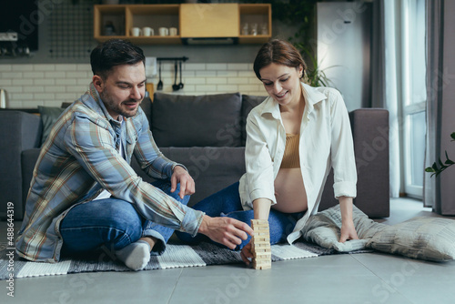 Young couple, man and pregnant woman, playing board game of jang together, sitting on the floor at home, having fun together photo