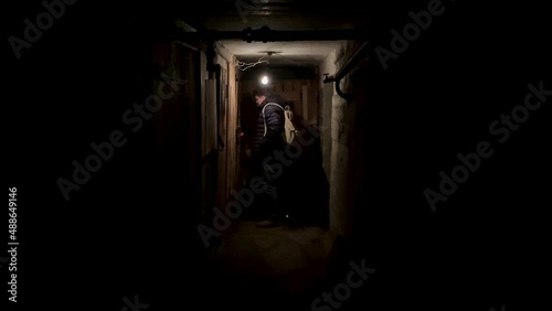  A man with a backpack in a dark basement closes the vault door with a padlock and leaves
