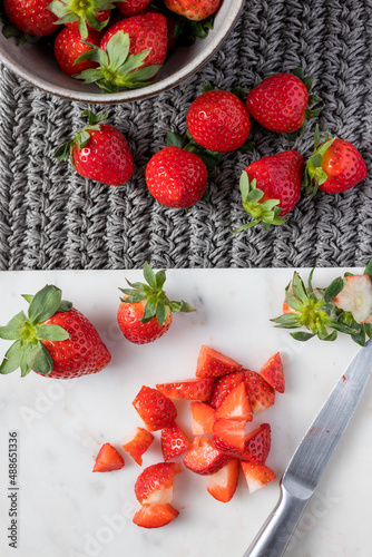 Strawberry pieces over a marble cutting board on a gray cotton background with more isolated shiny strawberries over it.