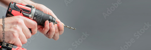 The man\'s hands install the drill into the drill, the hands take the drill and install it into the electric drill. Cordless tool on a gray background. DIY repair.