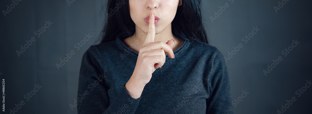 woman showing a sign of silence gesture putting finger in mouth - obrazy, fototapety, plakaty 