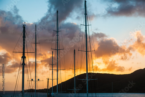Masts of sailing yachts against the backdrop of sea sunset near the mountains.