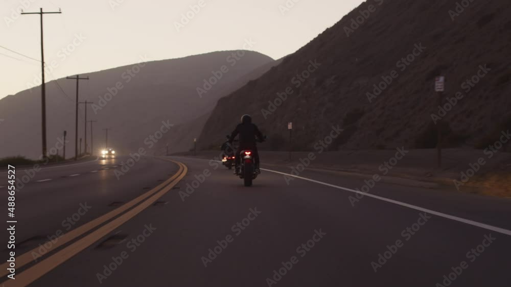 Pacific shore in Malibu with idyllic sunset sky above. Men ride beautiful black bikes on a highway with enormous mountain by the road. High quality 4k footage Pacific shore in Malibu with idyllic sunset sky above. Men ride beautiful black bikes on a highway with enormous mountain by the road. High quality 4k footage