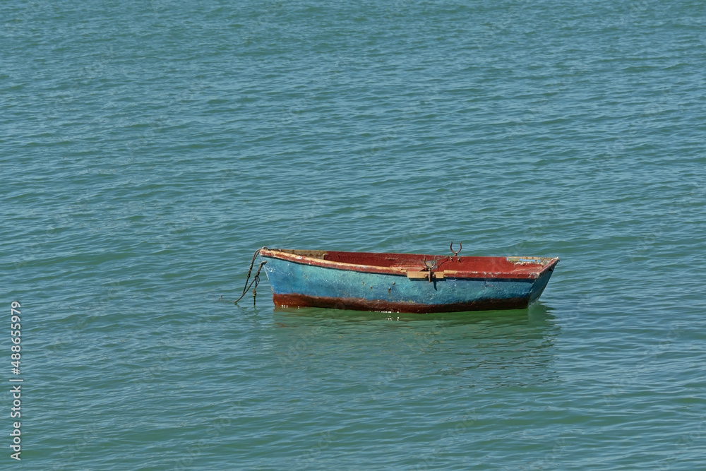 Old worn blue and red dinghy in the sea