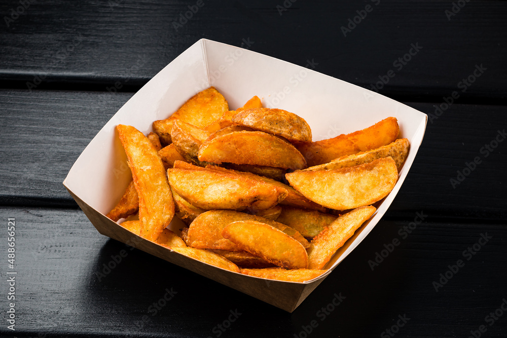 Rustic style golden crispy fried potato wedges sprinkled in box. Takeaway food in fast food restaurant Rustic style golden crispy fried potato wedges sprinkled in box. Takeaway food in fast food restaurant