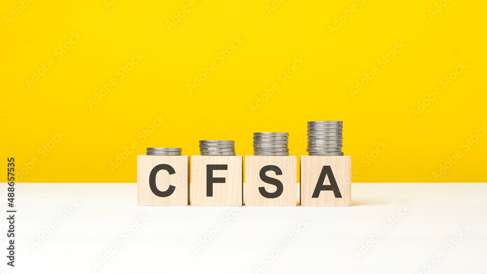 wooden cube on a concrete surface with text CFSA. copy space on right for design, yellow background wooden cube on a concrete surface with text CFSA. copy space on right for design, yellow background