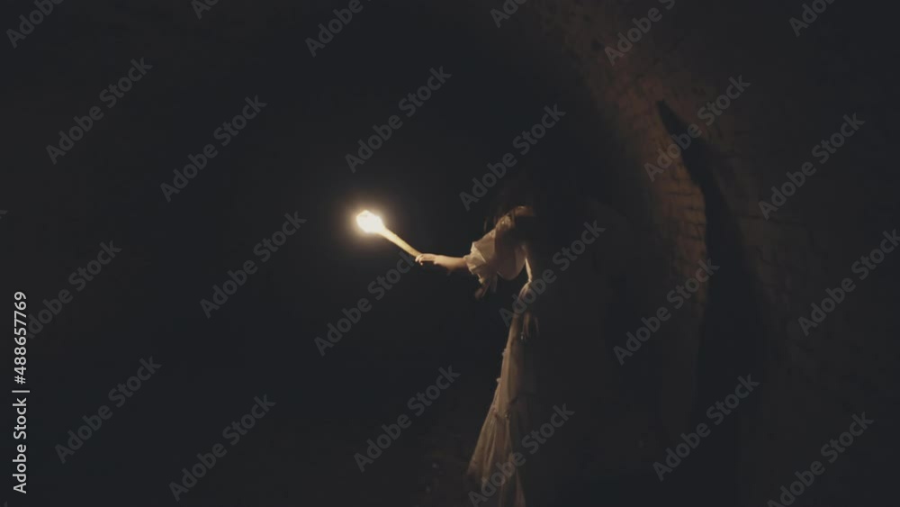 Woman with a torch in a vintage dress Runs through a medieval vVII century tunnel dungeon with brick vaults and a river.