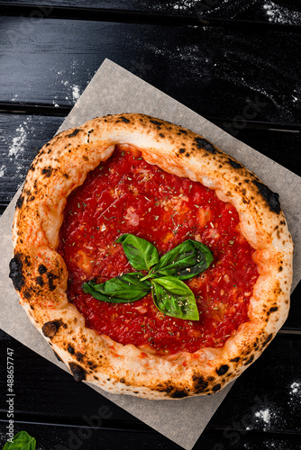 Traditional italian pizza with tomato sauce, garlic and basil on a wooden table