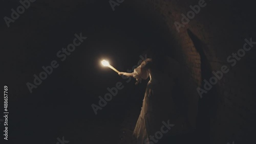 Woman with a torch in a vintage dress Runs through a medieval vVII century tunnel dungeon with brick vaults and a river.