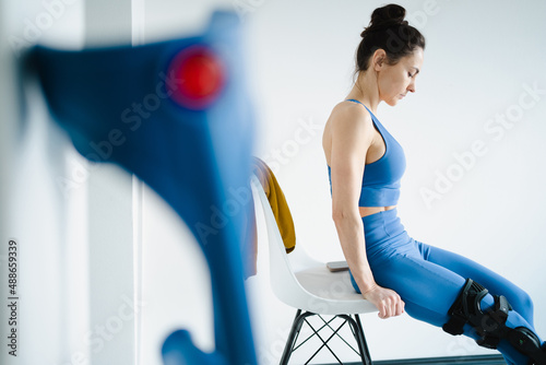 Sportliche Frau mit verletztem Knie macht Übungen auf dem Stuhl  photo