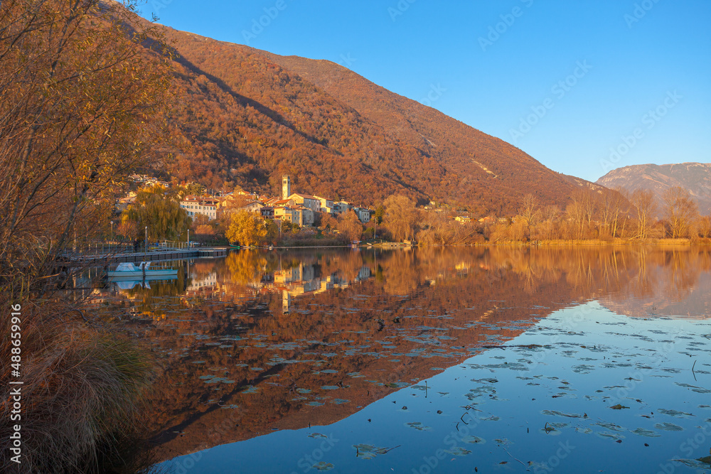 Small village of Santa Maria overlooking the lake during an autumn sunset. Revine Lakes, Veneto, Italy. Concept about reflection and relaxation