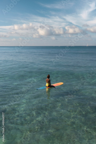 Charming curly African-American dark-skinned young woman  professional surfer sits on a long surfboard in the ocean  aerial shot from above