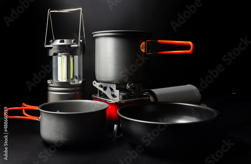 Fotografija Photo of titanium camping cookware with led lantern and portable gas stove on black backdrop
