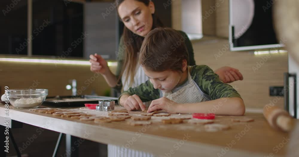 Young mother and son cooking cookies together in the kitchen. Mom and baby boy cut out homemade cookies with shapes form. Slow motion