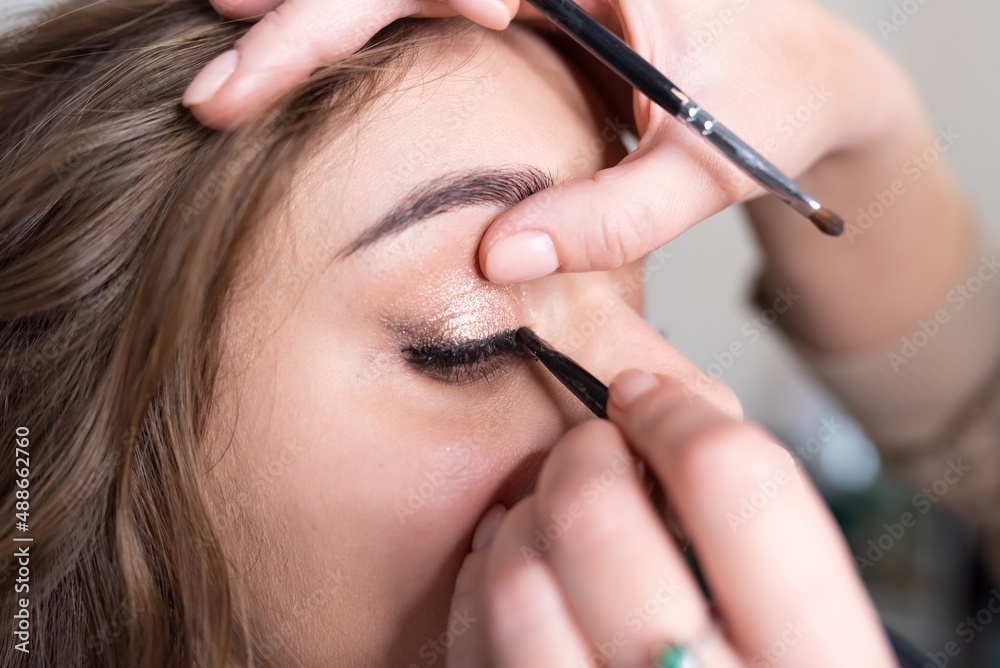 Make-up artist applies eyeliner to the girl's upper eyelid with a brush Make-up artist applies eyeliner to the girl's upper eyelid with a brush