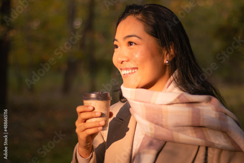 Wonderful young female model joyful in the park while having a coffee and watching the sunset in autumn.