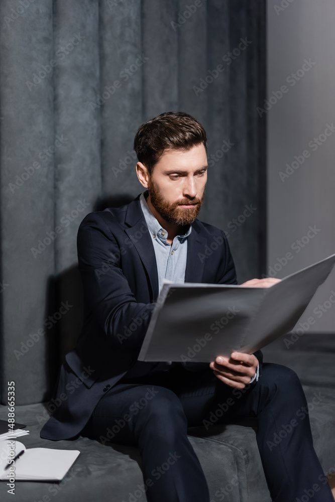 bearded businessman looking at folder while sitting in hotel lobby bearded businessman looking at folder while sitting in hotel lobby