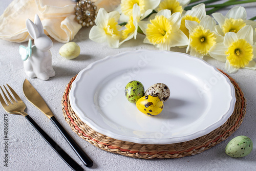 Easter table setting with daffodils, quail eggs and bunny on light gray table. Elegance dinner photo