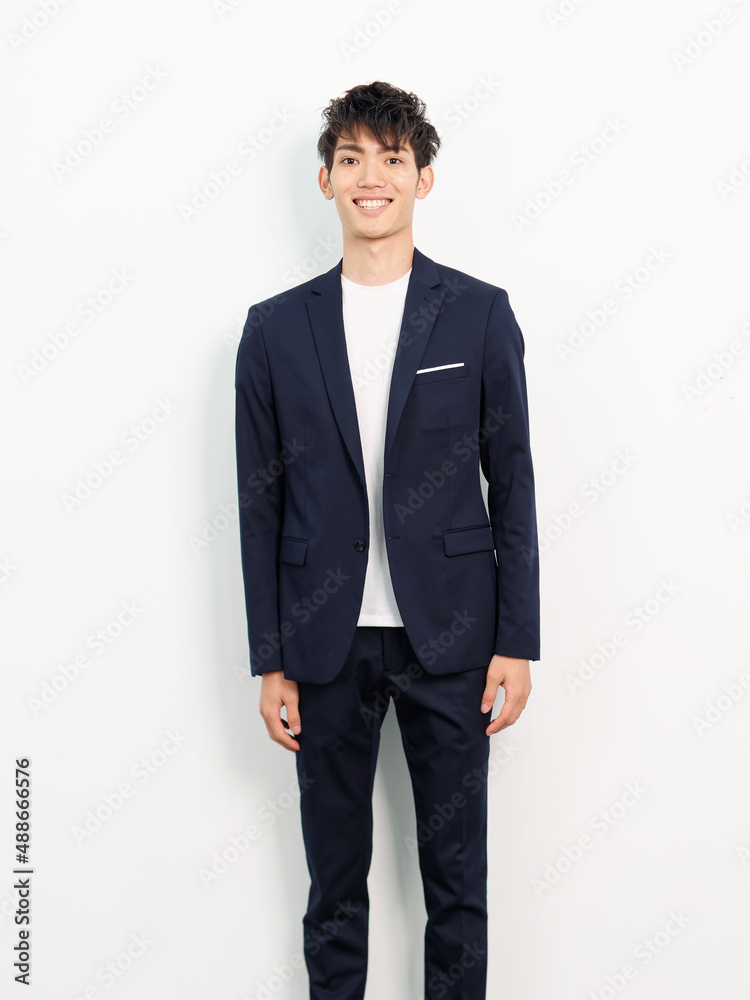 Portrait of handsome Chinese young man in dark blue leisure suit posing against white wall background. Hands on body sides and smiling at camera, looks confident. Portrait of handsome Chinese young man in dark blue leisure suit posing against white wall background. Hands on body sides and smiling at camera, looks confident.