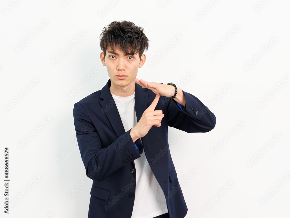 Portrait of handsome Chinese young man in dark blue leisure suit posing against white wall background. Finger point to palm to make stop gesture. Portrait of handsome Chinese young man in dark blue leisure suit posing against white wall background. Finger point to palm to make stop gesture.