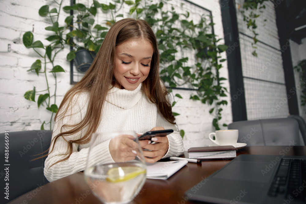 Woman sitting at table and using mobile phone . Girl holding smartphone surfing internet. Woman sitting at table and using mobile phone . Girl holding smartphone surfing internet.