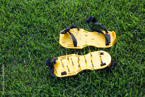Yellow lawn aerator sandals with nails for lawn cultivation. Shoes with aeration spikes for cultivation and revitalizing green grass of your garden