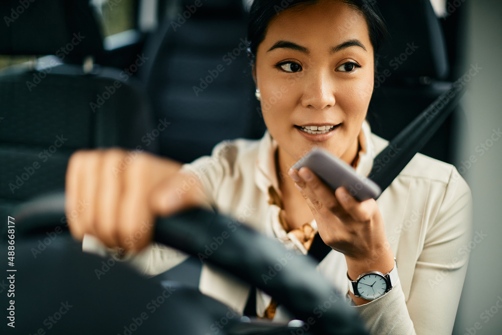 Young Asian woman sends voice message via smart phone while driving car.