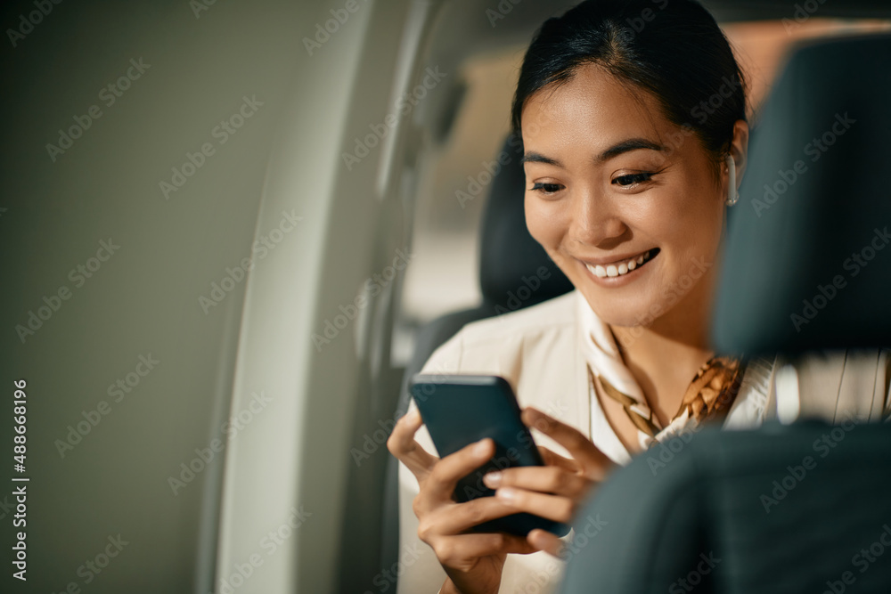 Happy Asian businesswoman uses smart phone while riding in a car.