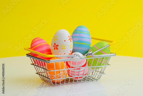 Shopping basket with colorful painted Easter eggs, minimal holiday season concept, yellow background, copy space