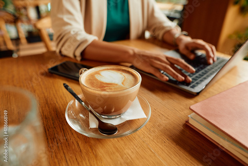 Close-up of cup of latte coffee with businesswoman working on laptop in background.