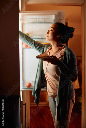 Young Asian woman takes food out of the fridge in the kitchen at night.