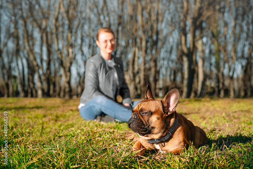 Woman with french bulldog dog sitting on grass in the park