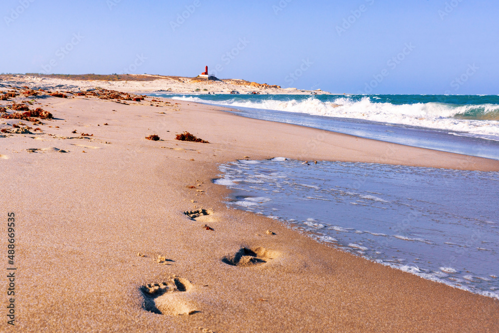 Footprints on the beach of Brazil with lighthouse in the back