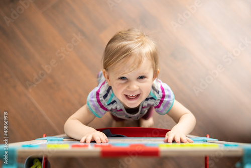 smiling happy two year old girl looking up at camera while standing next to easel magnetic board