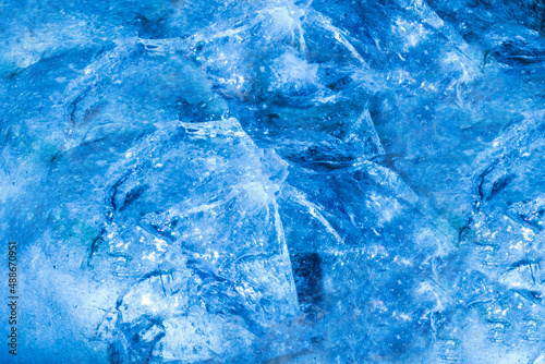 Close up photo of blue toned frozen cracked and damaged ice surface texture.