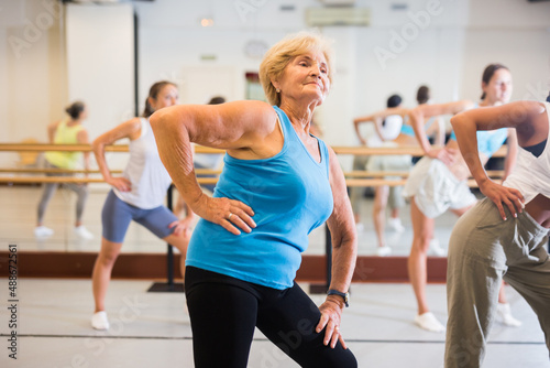 Portrait of smiling mature woman practicing ballet dance moves during group class in choreographic studio
