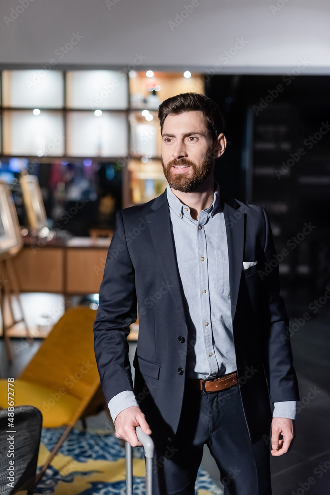 bearded man in suit holding luggage handle in hotel foyer bearded man in suit holding luggage handle in hotel foyer
