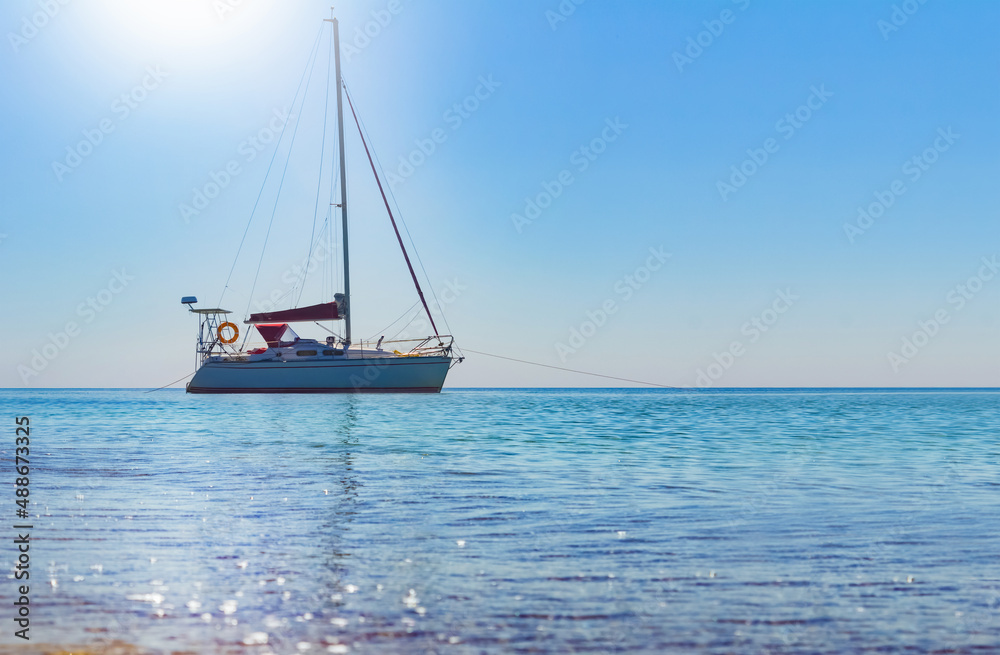 Photo of white colored sailboat with lowered sails drifting in mid day open sea. Photo of white colored sailboat with lowered sails drifting in mid day open sea.