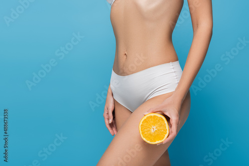 cropped view of slim woman in white panties holding orange isolated on blue