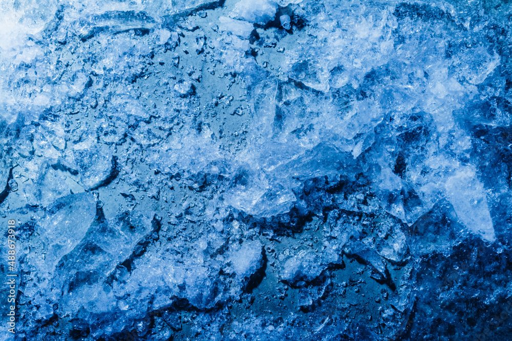 Photo of blue toned frozen cracked ice with snow particles surface texture.