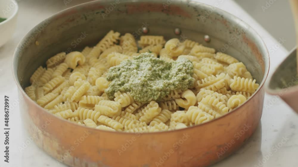 Crop cook adding pesto sauce in pot with pasta Crop cook adding pesto sauce in pot with pasta