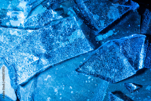 Photo of blue toned frozen cracked ice pieces surface texture.
