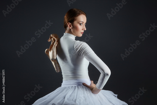 portrait of a ballerina holding pointe shoes. photo shoot in the studio on a dark background