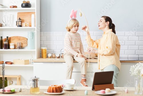 Portrait of young woman decorating house for Easter with cute little boy wearing bunny ears, copy space photo