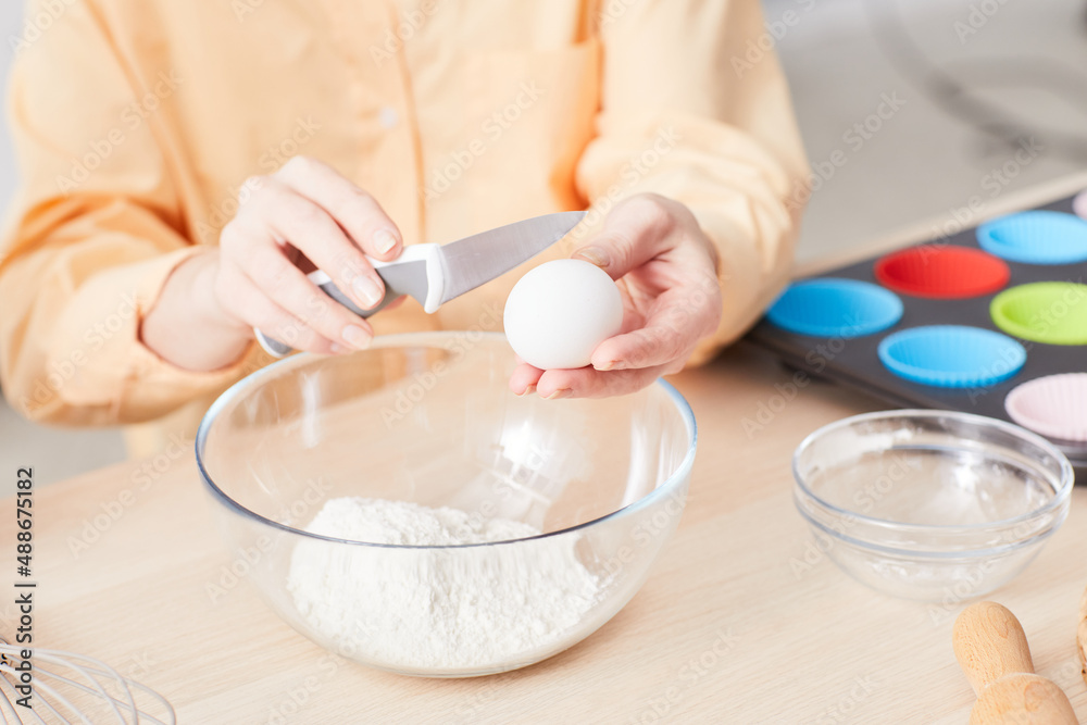 Close up of young woman breaking eggs while baking homemade muffins in kitchen, copy space Close up of young woman breaking eggs while baking homemade muffins in kitchen, copy space