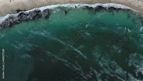 Top down aerial shot flying forward over Camps Bay beach with a kitesurfer riding the waves